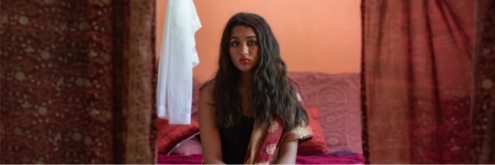 A young woman sitting on the edge of her bed