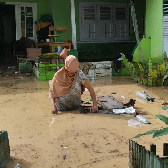 A woman up to her waist in muddy floodwater attempting to retrieve items from outside her home.