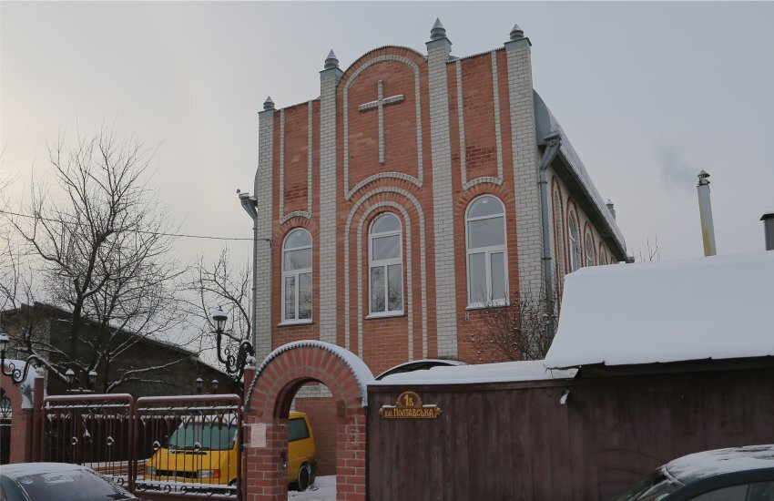 Large red brick church building with fence snow on vehicles outside